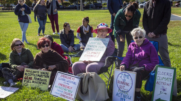 Group of people with protest signs sitting on grass.